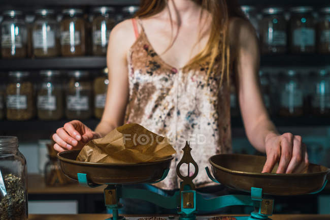 Mujer de pie cerca de viejas escamas con bolsa de papel en la tienda de especias - foto de stock
