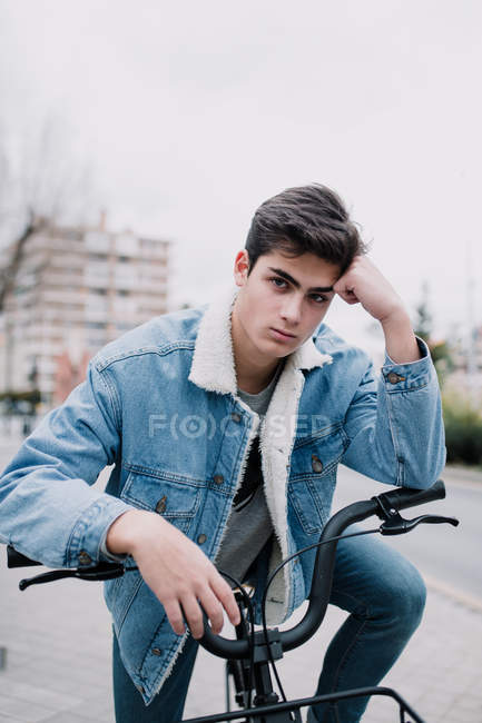 Молодой красивый подросток опирается на велосипедный руль и смотрит в камеру на улице — стоковое фото