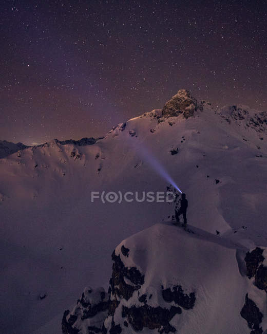 Unrecognizable hiker with light on head standing on mountain covered with snow at night — Stock Photo