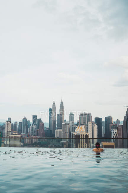 Vista posteriore della donna che nuota in piscina sullo sfondo dei grattacieli della città. — Foto stock