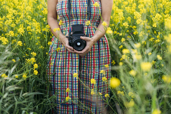 Femme en robe colorée tenant appareil photo dans la nature — Photo de stock
