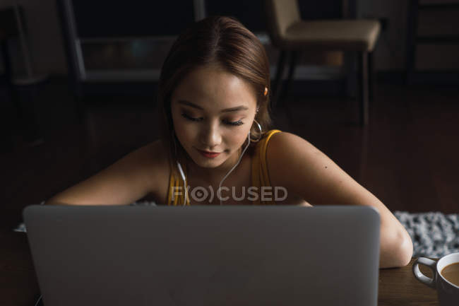 Молода азіатка використовує ноутбук з навушниками за столом — стокове фото