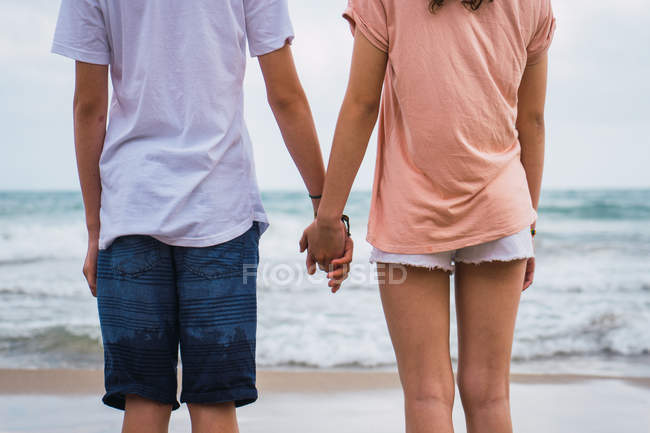 Teenager friends standing and holding hands on beach — Stock Photo