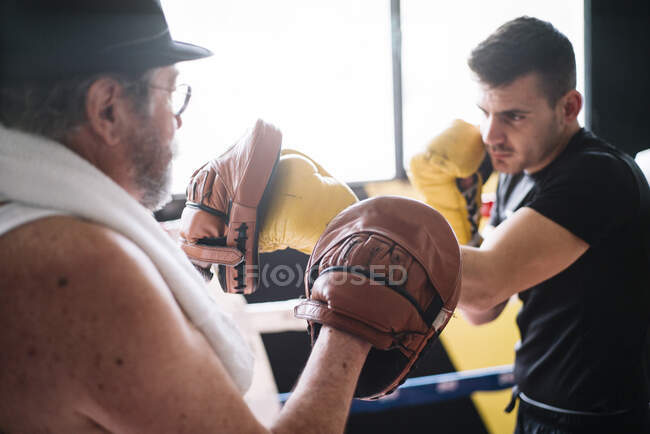 Side view of boxer man punching gloves of trainer in the gym. — Stock Photo