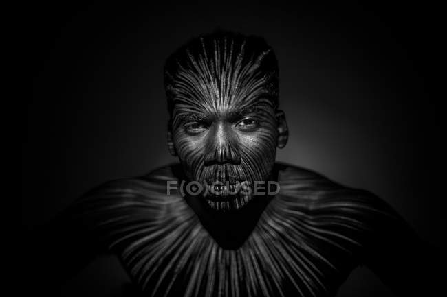 Emotionsloser ethnischer Mann mit hellen Linien am Körper und Blick in die Kamera — Stockfoto