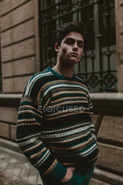 Young confident teenager in sweater walking on city street and looking at camera — Stock Photo