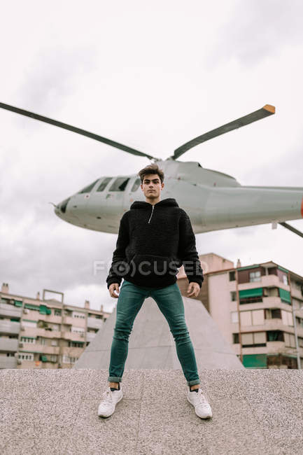 Bel giovanotto in piedi di fronte al monumento elicottero sulla strada della città — Foto stock
