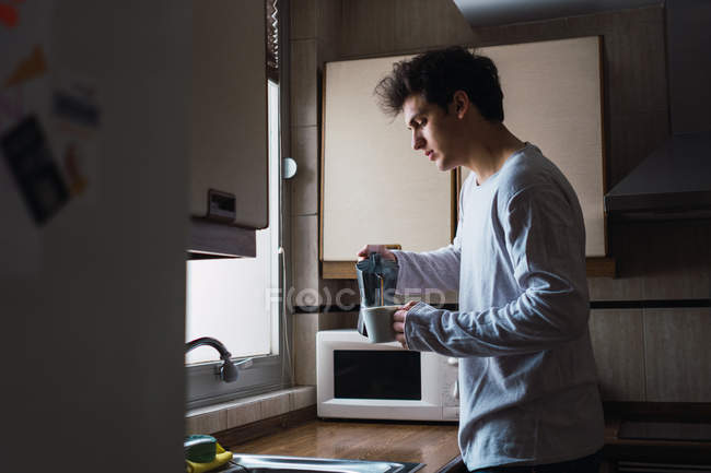 Uomo in pigiama versare il caffè in tazza in cucina — Foto stock