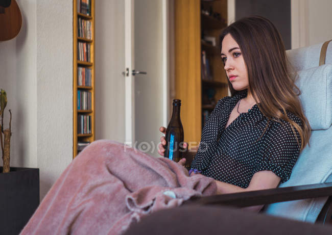 Jovem mulher pensativa com cerveja descansando em poltrona — Fotografia de Stock