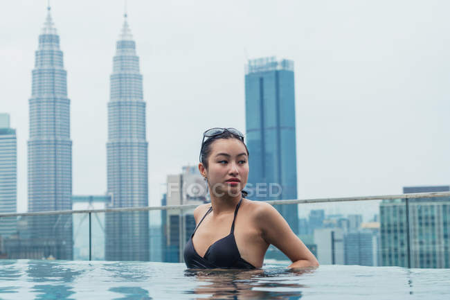 Donna asiatica rilassante in piscina con grattacieli sullo sfondo — Foto stock