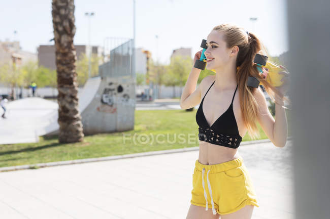 Blonde girl standing with penny board on sidewalk in summer — Stock Photo