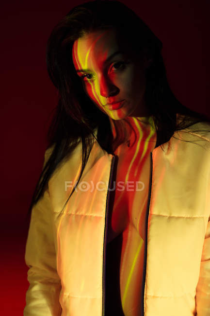 Mulher bonita em jaqueta branca com manchas de luz no rosto olhando para a câmera — Fotografia de Stock