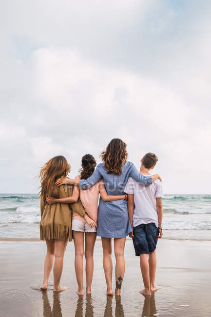 Woman and teenagers hugging together on seashore — Stock Photo