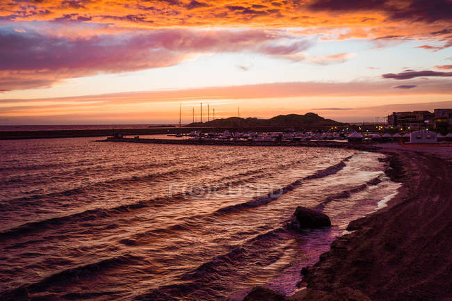 Cielo dramático al atardecer y ciudad en la costa, Cerdeña, Italia - foto de stock