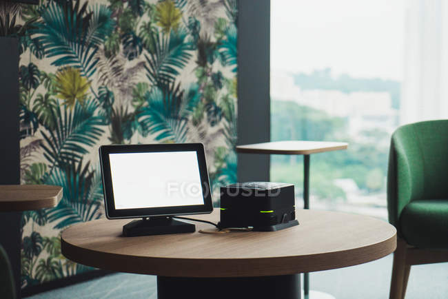 Monitor em branco e pequena unidade de sistema do PC moderno na mesa redonda de madeira no quarto elegante — Fotografia de Stock
