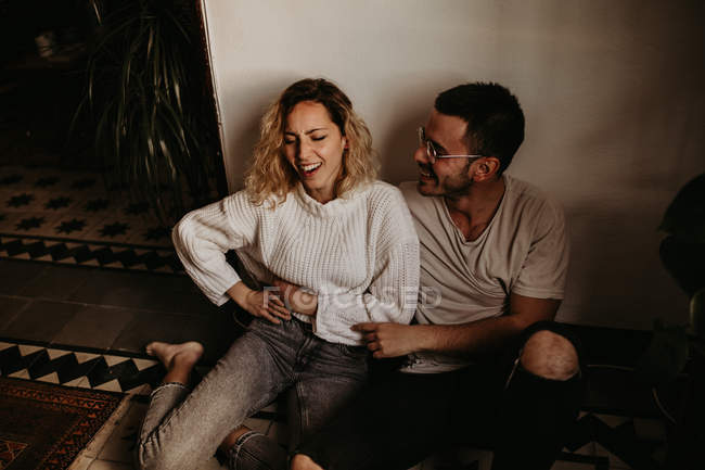 Hombre y mujer alegres sentados en el suelo y divirtiéndose en casa - foto de stock