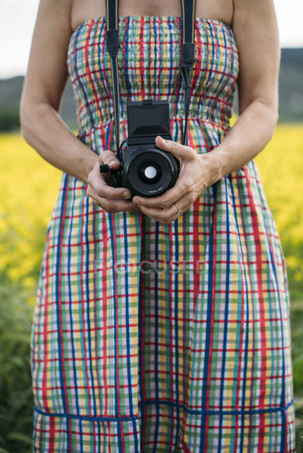 Mulher em vestido colorido segurando dispositivo de foto na natureza — Fotografia de Stock