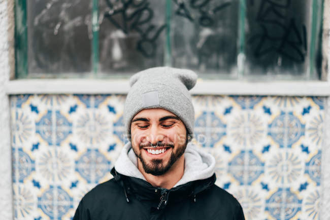 Retrato de alegre animado turista masculino em pé na parede com azulejos azuis — Fotografia de Stock