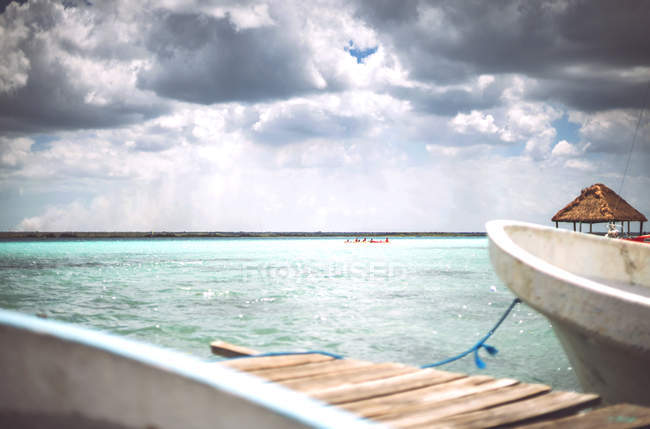 Stormy clouds floating over clean Caribbean sea and small pier with boat, Mexico — Stock Photo