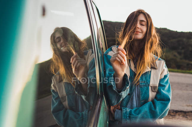 Bella giovane donna appoggiata sulla macchina e toccando i capelli in natura — Foto stock