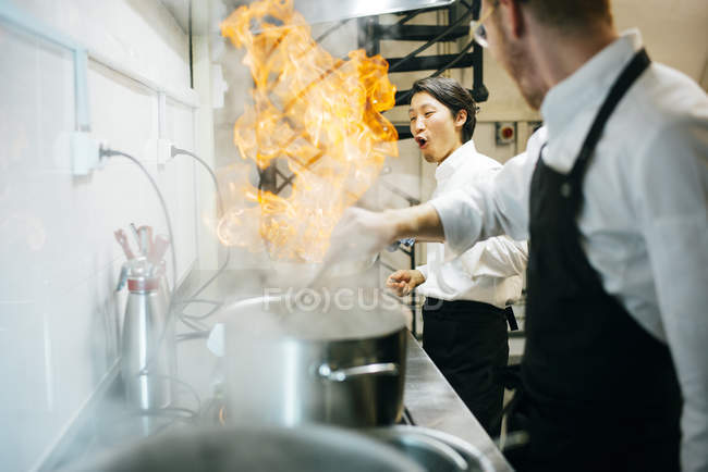 Happy cook making a flambe in restaurant kitchen with colleague watching — Stock Photo