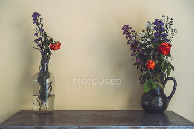 Floreros con flores en la mesa delante de la pared - foto de stock