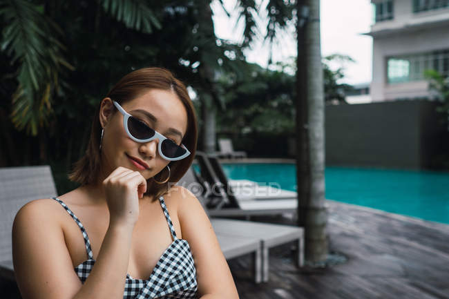 Retrato de mulher bonita em óculos de sol em pé na piscina — Fotografia de Stock