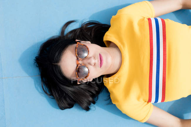 Женщина в спортивной одежде и солнечных очках лежит на синем фоне — стоковое фото