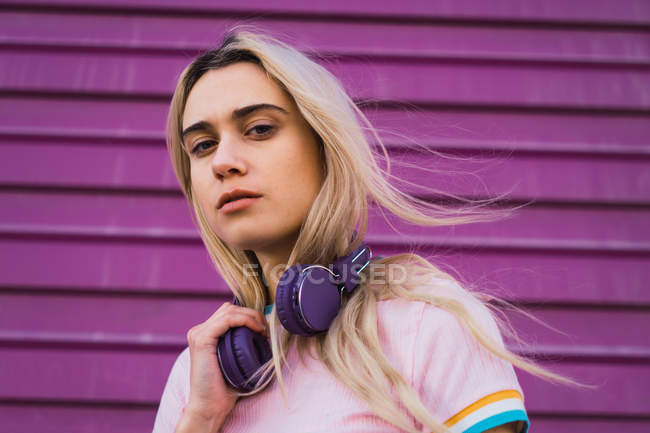 Retrato de mujer rubia joven con auriculares púrpura contra la pared púrpura - foto de stock