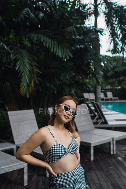 Portrait de Jolie femme en lunettes de soleil debout à la piscine — Photo de stock