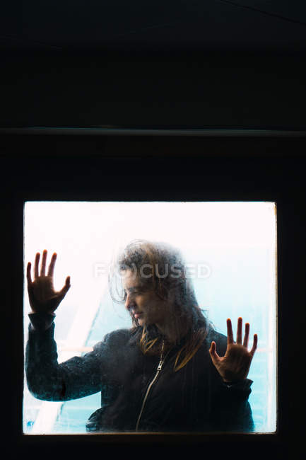 Mujer bastante joven apoyada en la ventana fuera de la habitación oscura - foto de stock