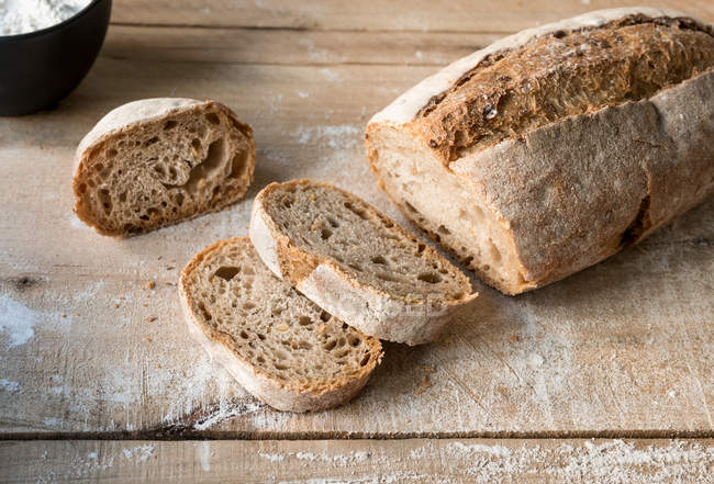Pane parzialmente affettato e appetitoso in farina su tavola di legno grezzo — Foto stock