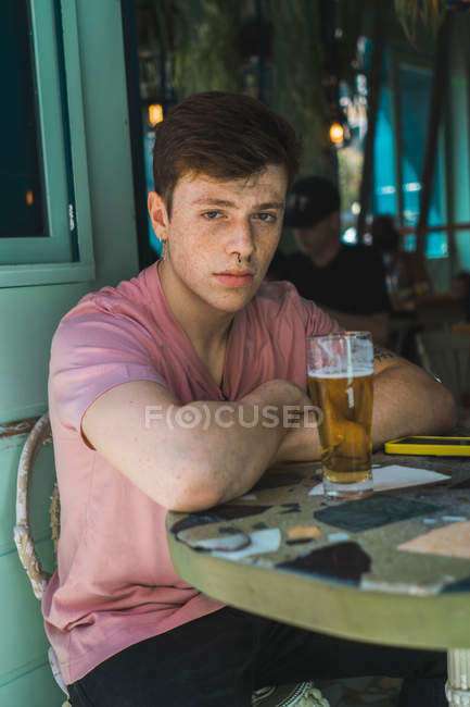 Jovem confiante sentado com um copo de cerveja à mesa — Fotografia de Stock