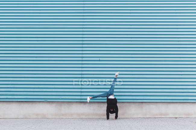 Unrecognizable man standing on hands at blue metal wall — Stock Photo
