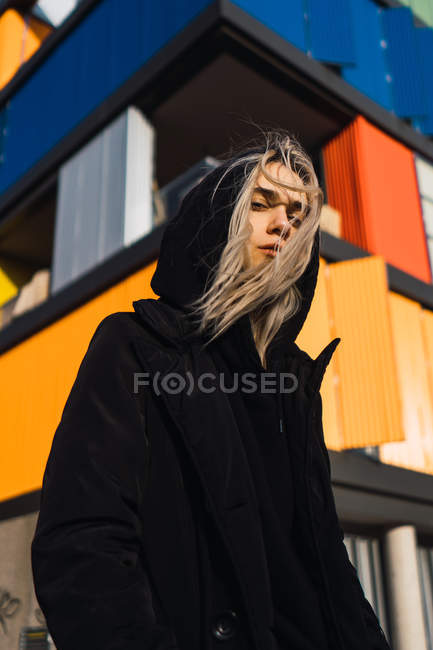 Mulher loira atraente olhando para a câmera contra edifício colorido — Fotografia de Stock