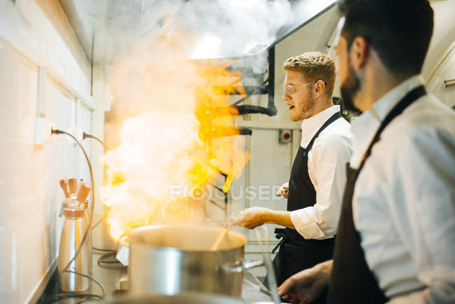 Cuoco felice fare un flambe in cucina ristorante con collega a guardare — Foto stock
