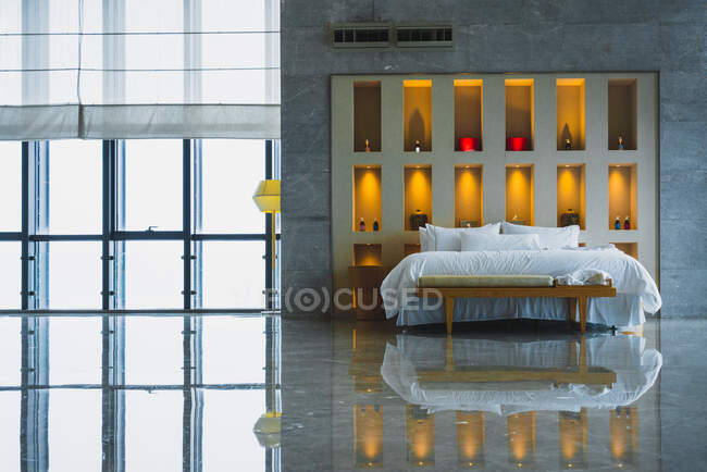 Интерьер современной просторной спальни с каменным блестящим полом и огромной кроватью против декоративной освещенной стены, Чунцин собственности — стоковое фото