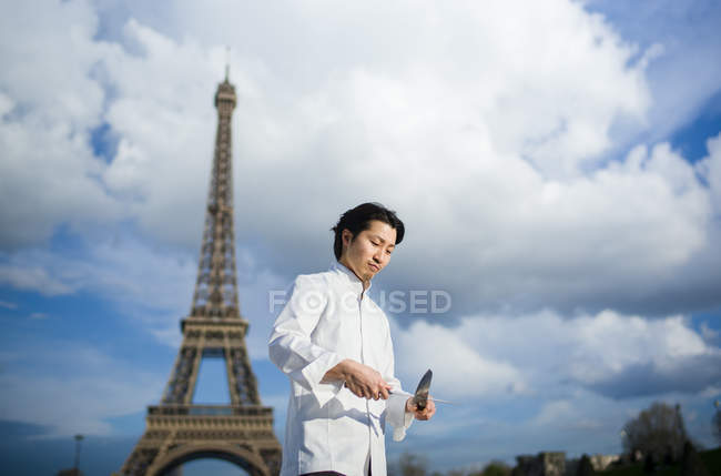 Japanese chef with knives standing in front of Eiffel Tower in Paris — Stock Photo