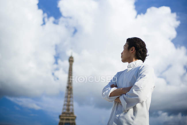 Chef japonés con los brazos cruzados de pie frente a la Torre Eiffel en París - foto de stock