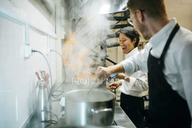 Glücklicher Koch, der in der Restaurantküche mit Kollegen Flammkuchen kocht — Stockfoto