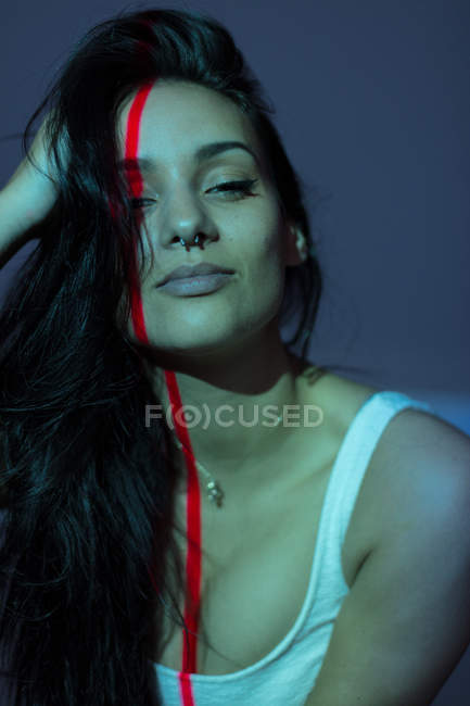 Jeune femme attrayante avec ligne rouge sur le visage en regardant la caméra sur fond sombre — Photo de stock