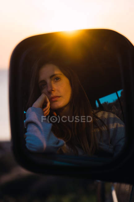 Spiegelbild einer nachdenklichen Touristin, die bei Sonnenuntergang im Auto sitzt — Stockfoto