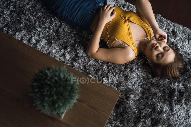 Relaxed woman with earphones lying on carpet — Stock Photo