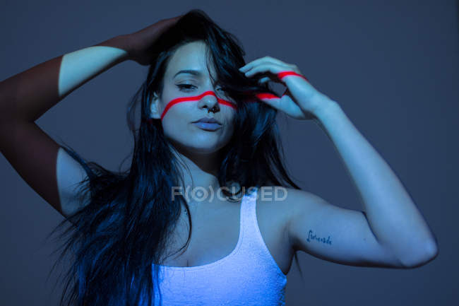 Jeune femme attrayante avec ligne rouge sur le visage et le corps en regardant la caméra sur fond sombre — Photo de stock