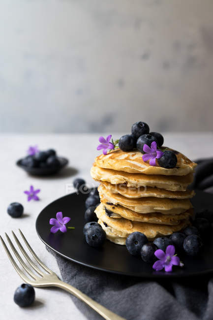 Стопка аппетитных вкусных печенек с черникой и фиолетовыми цветами на черной тарелке — стоковое фото