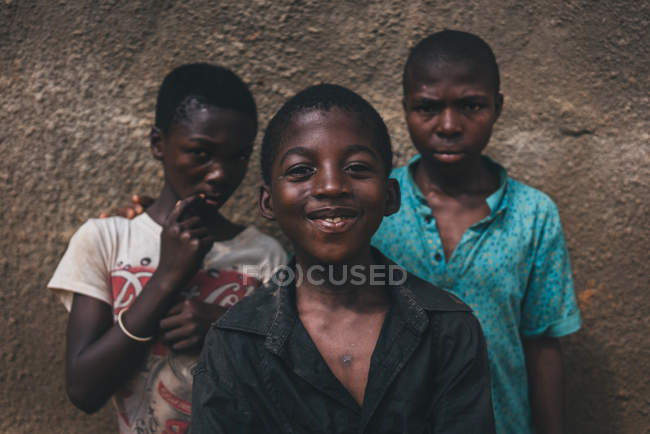 КАМЕРУН - АФРИКА - 5 апреля 2018 года: Веселые крепкие африканские мальчики стоят у грубой стены и смотрят в камеру — стоковое фото