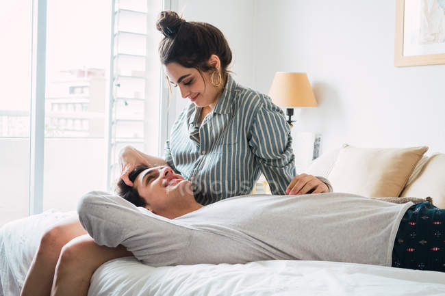 Fröhlicher junger Mann liegt auf Knien seiner Freundin zu Hause im Bett — Stockfoto