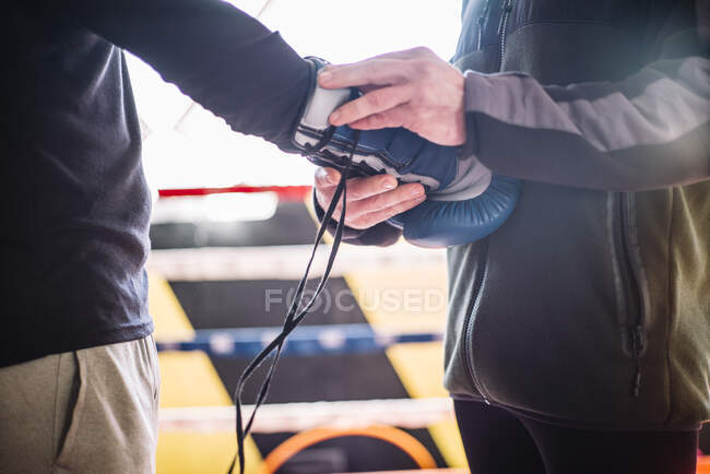 Cortar pessoa irreconhecível ajudando a desportista com luva de boxe no ringue. — Fotografia de Stock