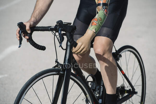 Homem de colheita com braço artificial andar de bicicleta na estrada de asfalto durante a corrida — Fotografia de Stock