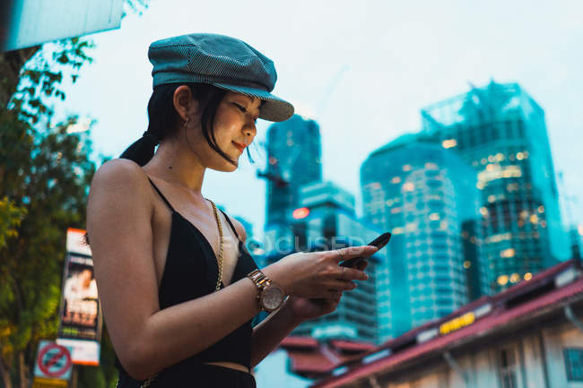 Mujer asiática en ropa elegante usando teléfono inteligente en la calle en la ciudad - foto de stock